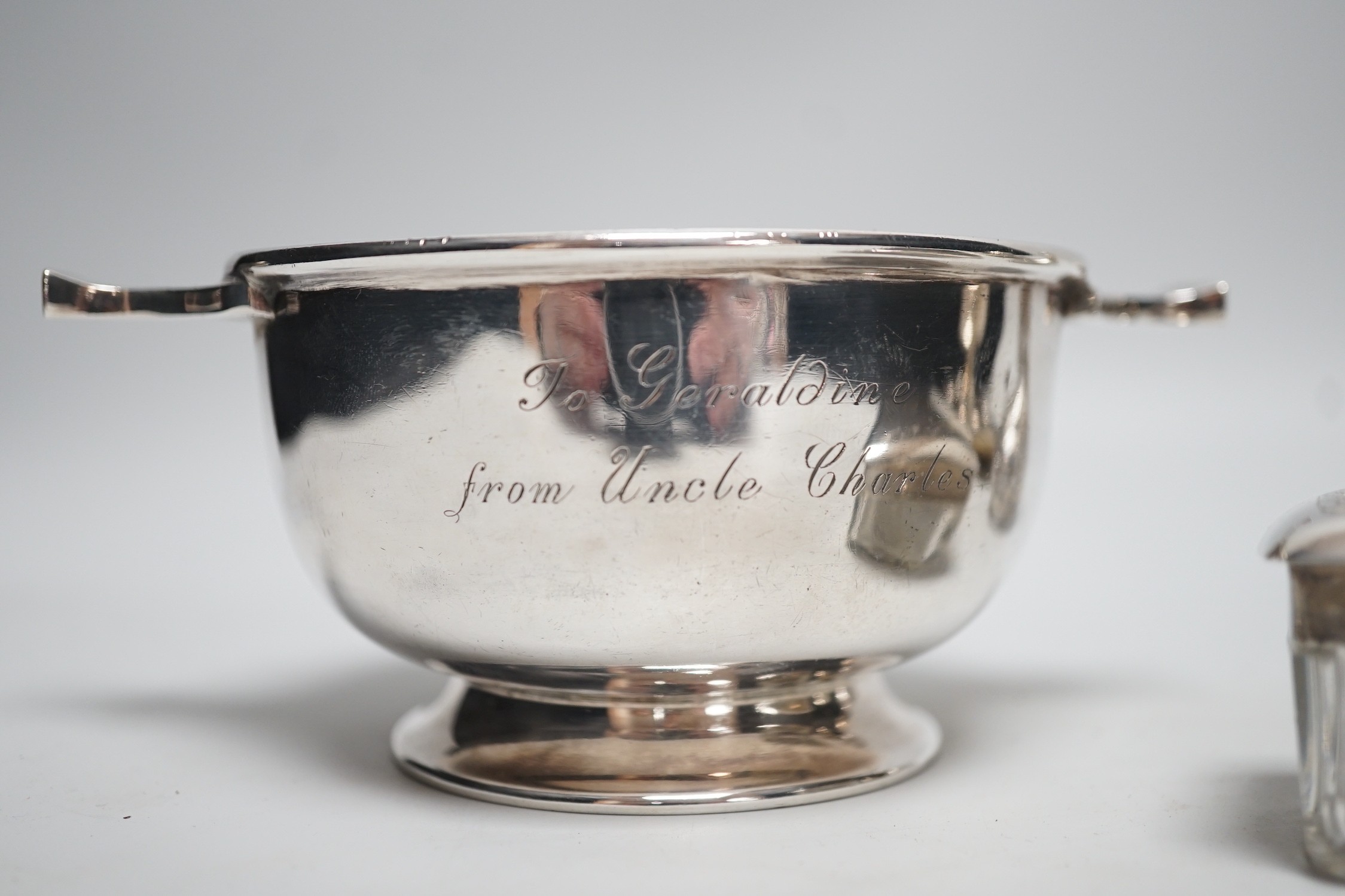 A George V silver two handled bowl, 14.6cm over handles, a white metal overlaid glass scent bottle (a.f.), a silver mounted blotter and a silver mounted glass toilet jar.